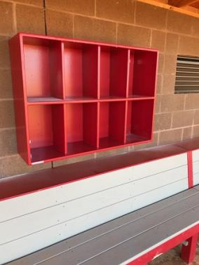 A red 8 helmet cubby rack mounted on a wall, designed to hold baseball or softball helmets, with visible individual compartments.