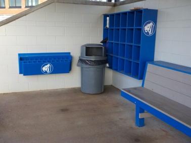 A blue 24 Helmet Cubby Rack installed outdoors, with the rack's individual compartments visible and a bench to the right.