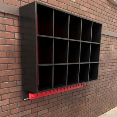 A black dugout storage rack with multiple compartments for helmets and bats, mounted on a brick wall.