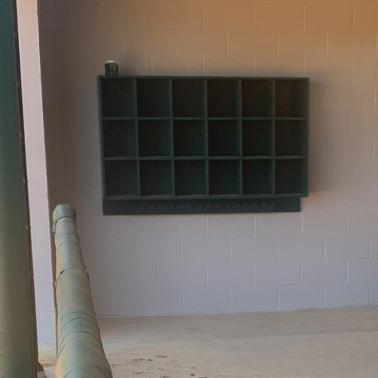A black dugout storage rack mounted on a wall designed to hold baseball or softball helmets, featuring three rows of six compartments.