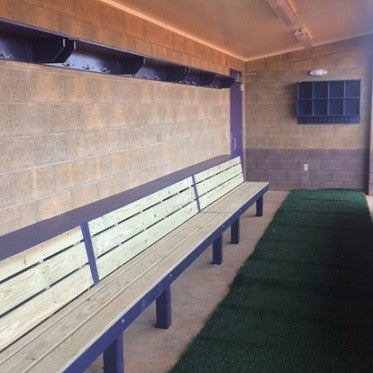 A Player Shelf in a dugout, featuring wooden slatted bench seating with a solid color wall behind and artificial grass flooring.