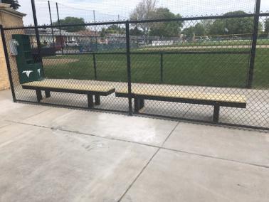 Two benches behind a chain-link fence with a sports field in the background