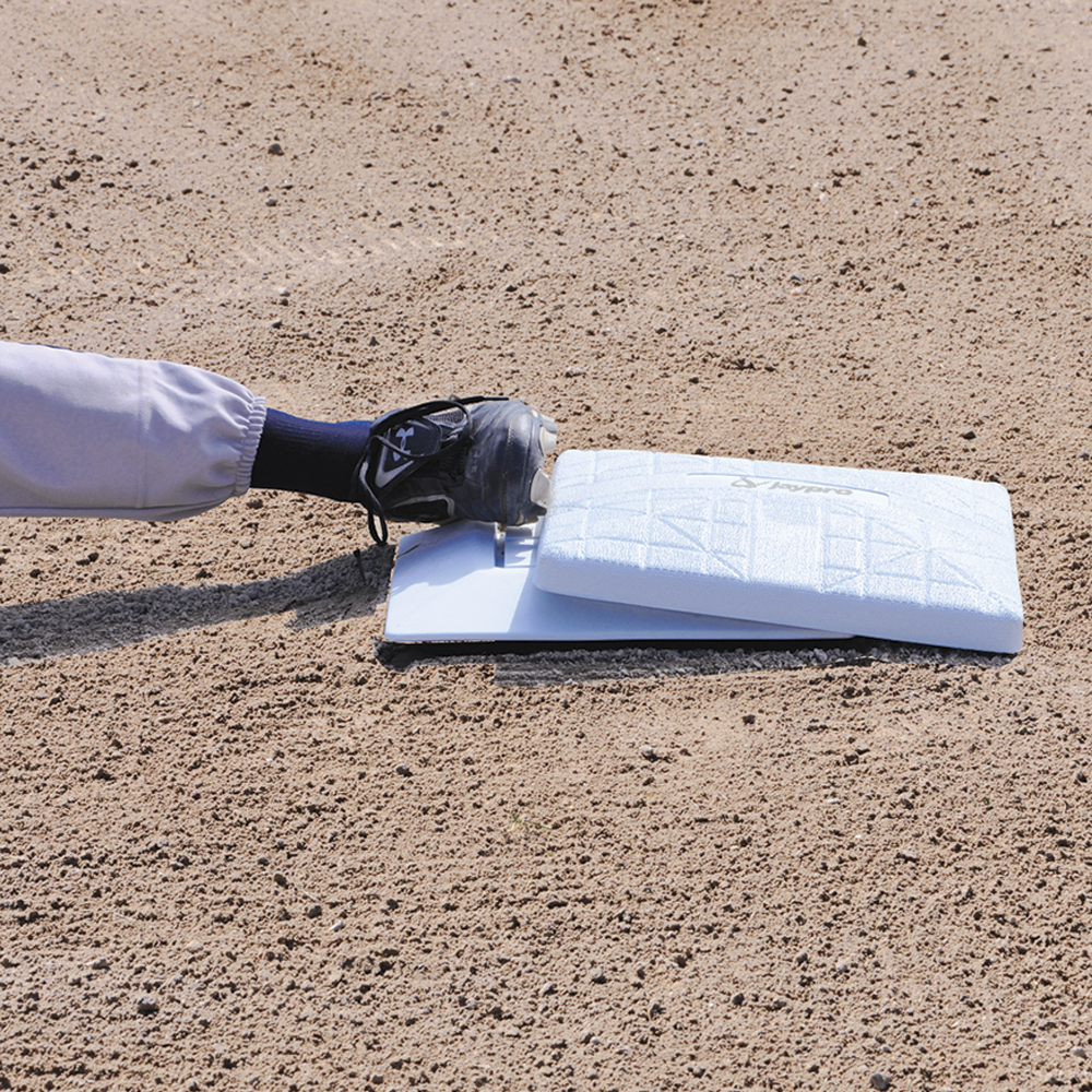 Baseball player sliding with just his leg and cleats showing into a white jaypro base with dirt surrounding. 